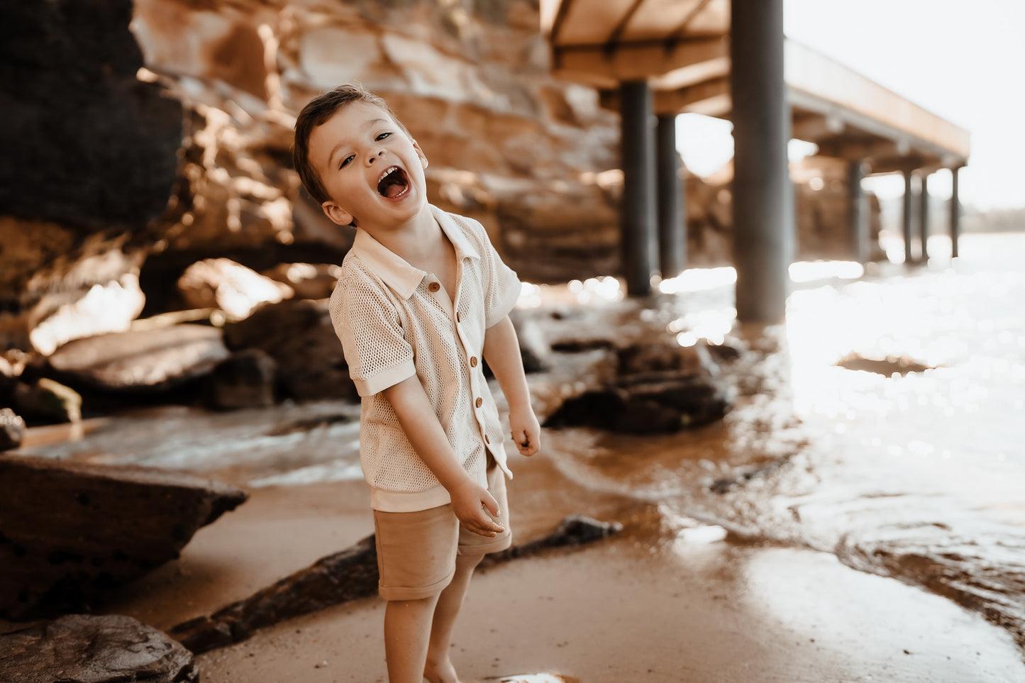Australia's newest surf and skate clothing brand for boys aged 1-8. Boy standing under jetty wearing a vintage tan mesh shirt by Kohvi on the Central Coast, Austalia.