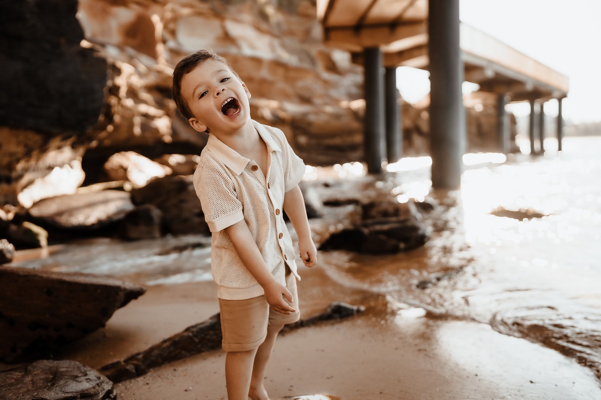 Australia's newest surf and skate clothing brand for boys aged 1-8.  Boy standing under jetty wearing a vintage tan mesh shirt by Kohvi on the Central Coast, Austalia.